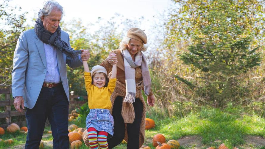 Two grandparents walking with granddaughter hand-in-hand in autumn