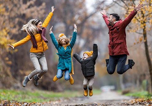 Family of four outdoors in autumn jumping and smiling